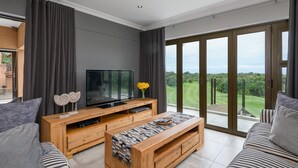 A modern living room with a large flat-screen TV, wooden entertainment unit, and a sofa. - San Lameer Villa Rentals 14109 (Southbroom)