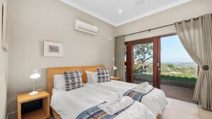 A bedroom with a large bed, a nightstand, a bedside lamp, an air conditioning unit, and a view of the outdoors through a glass door. - San Lameer Villa Rentals 14205 (Southbroom)