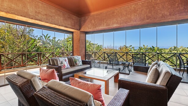 A spacious balcony with wicker furniture, a glass-top table, and a view of greenery. - San Lameer Villa Rentals 14205 (Southbroom)