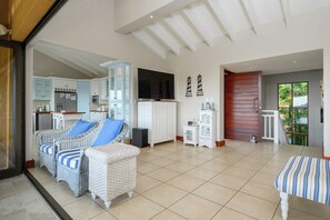Uma sala de estar ampla com móveis de vime, uma televisão de tela plana e vista para o exterior.