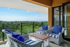 A balcony with wicker furniture, a wooden table, and a view of a lush landscape.