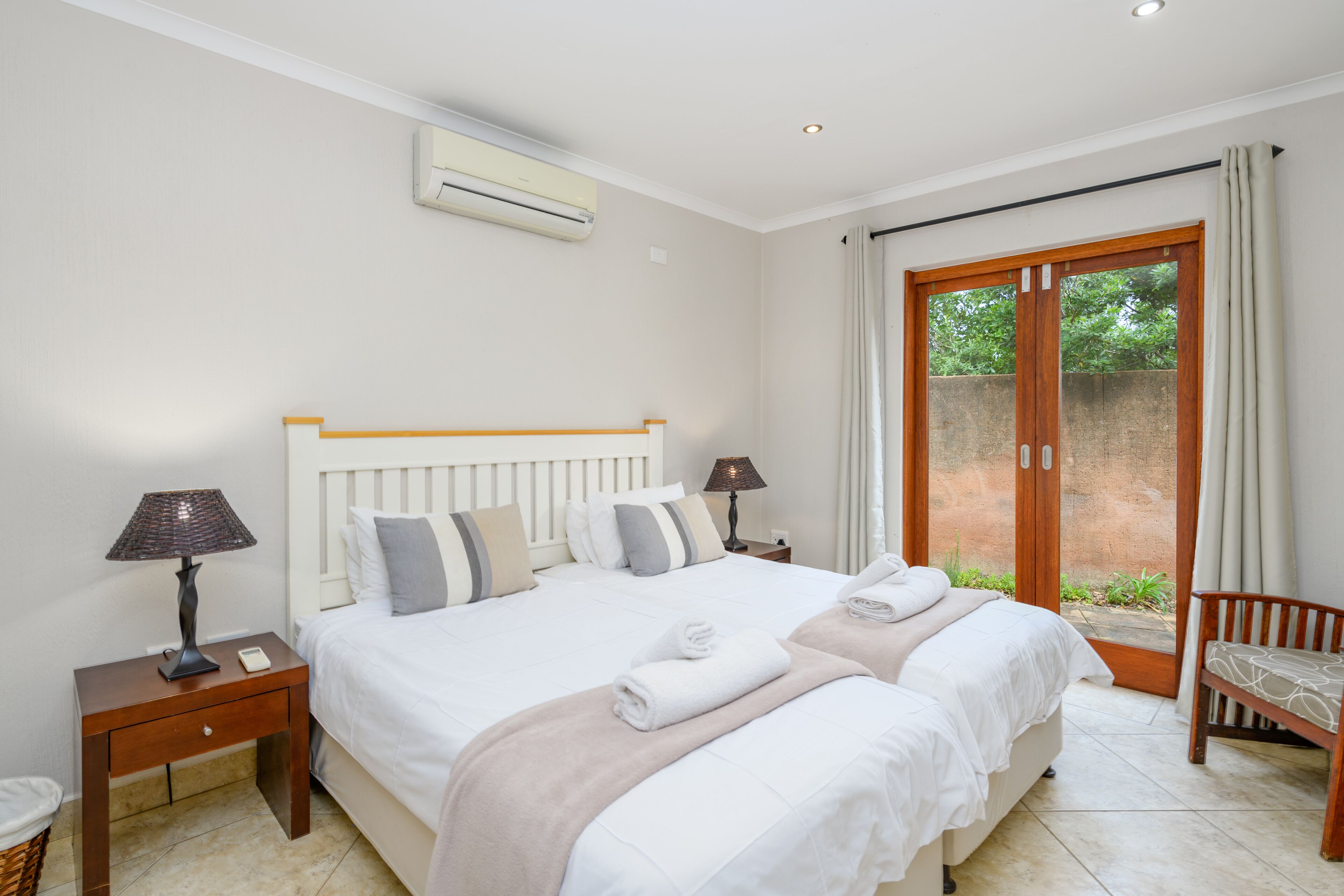 A bedroom with a large bed, two bedside tables, a lamp, a chair, and a sliding glass door to the outside.