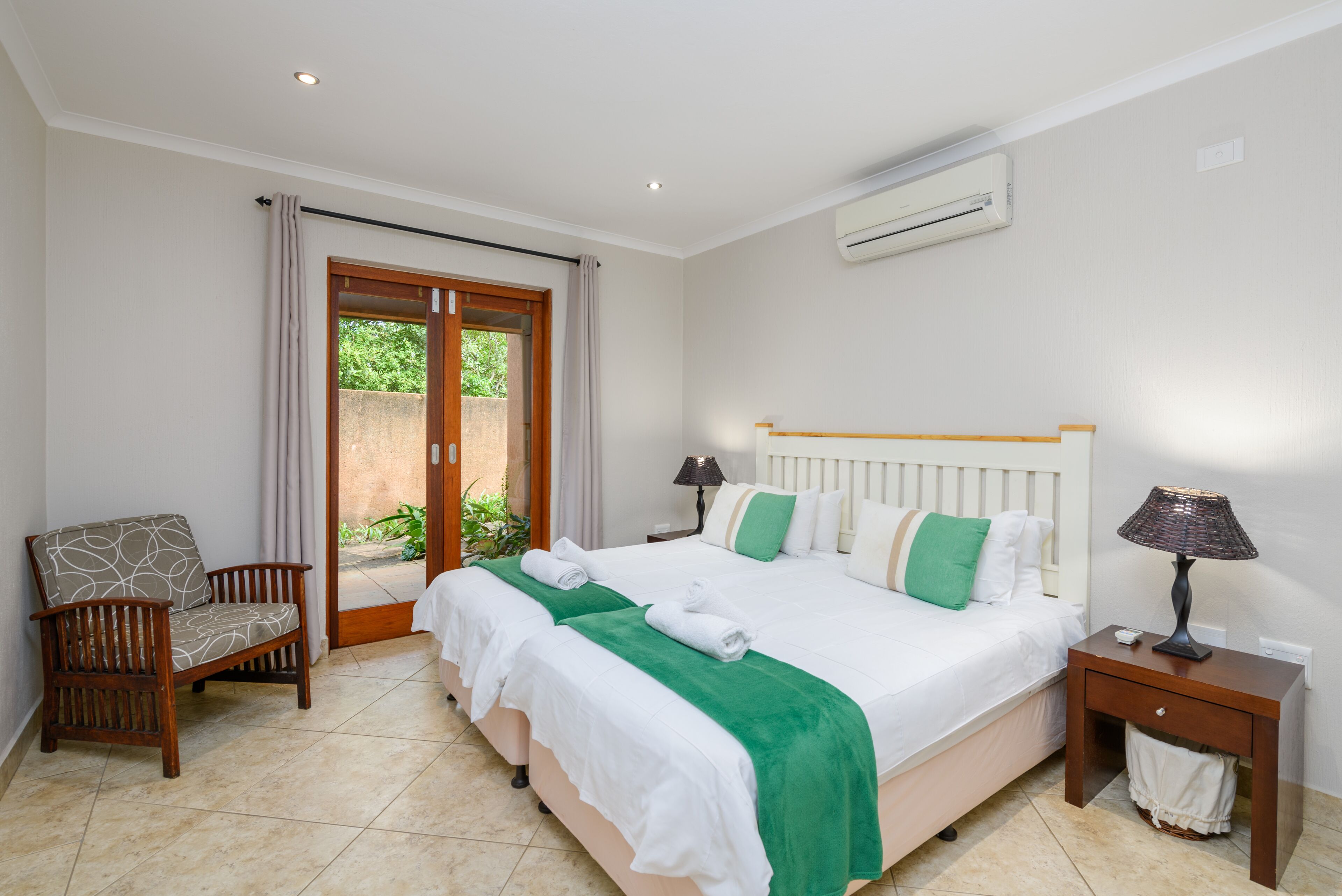 A bedroom with a bed, a chair, a nightstand, and an air conditioning unit.