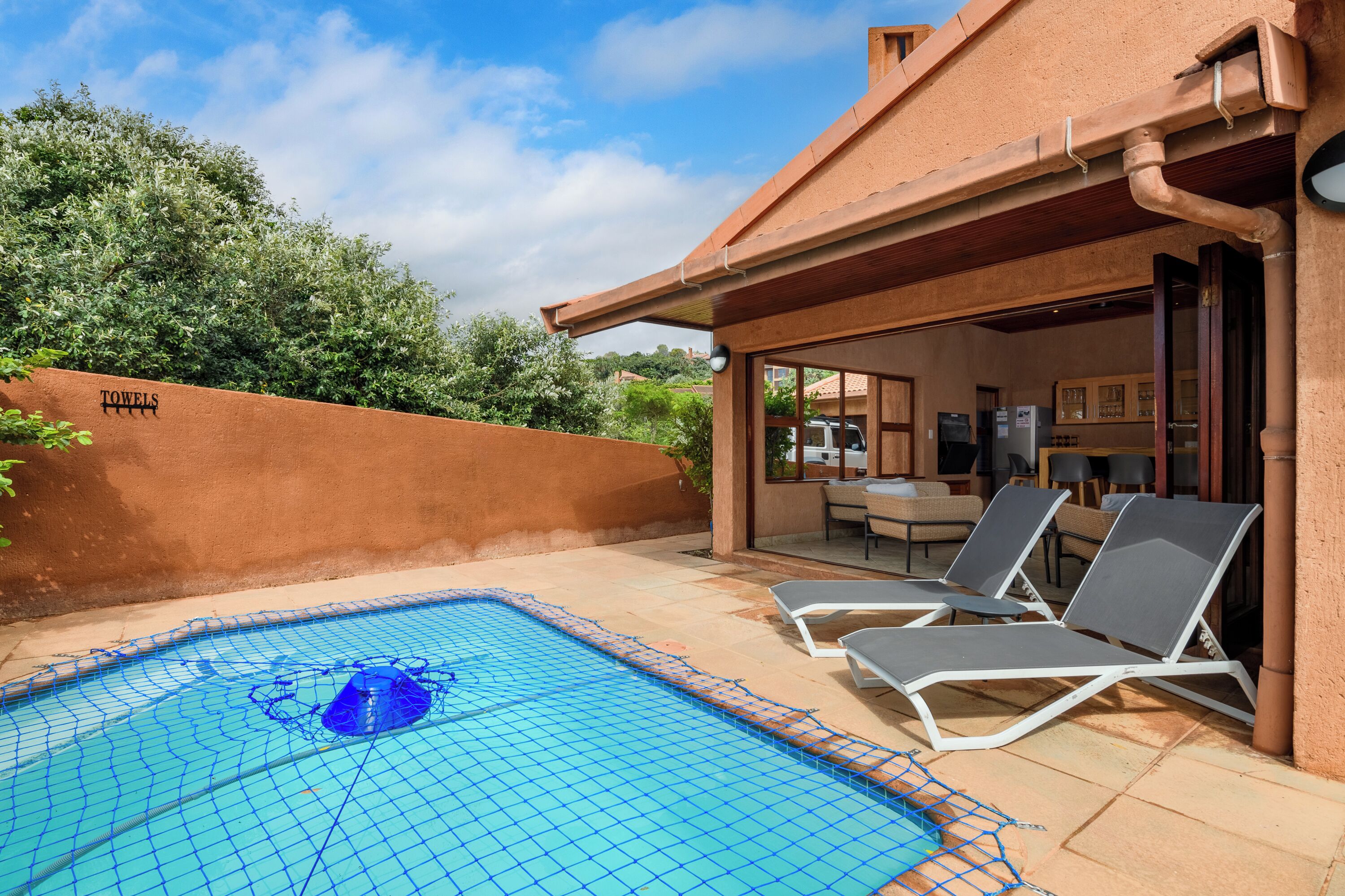 A swimming pool with a blue net, lounge chairs, and a covered patio area.
