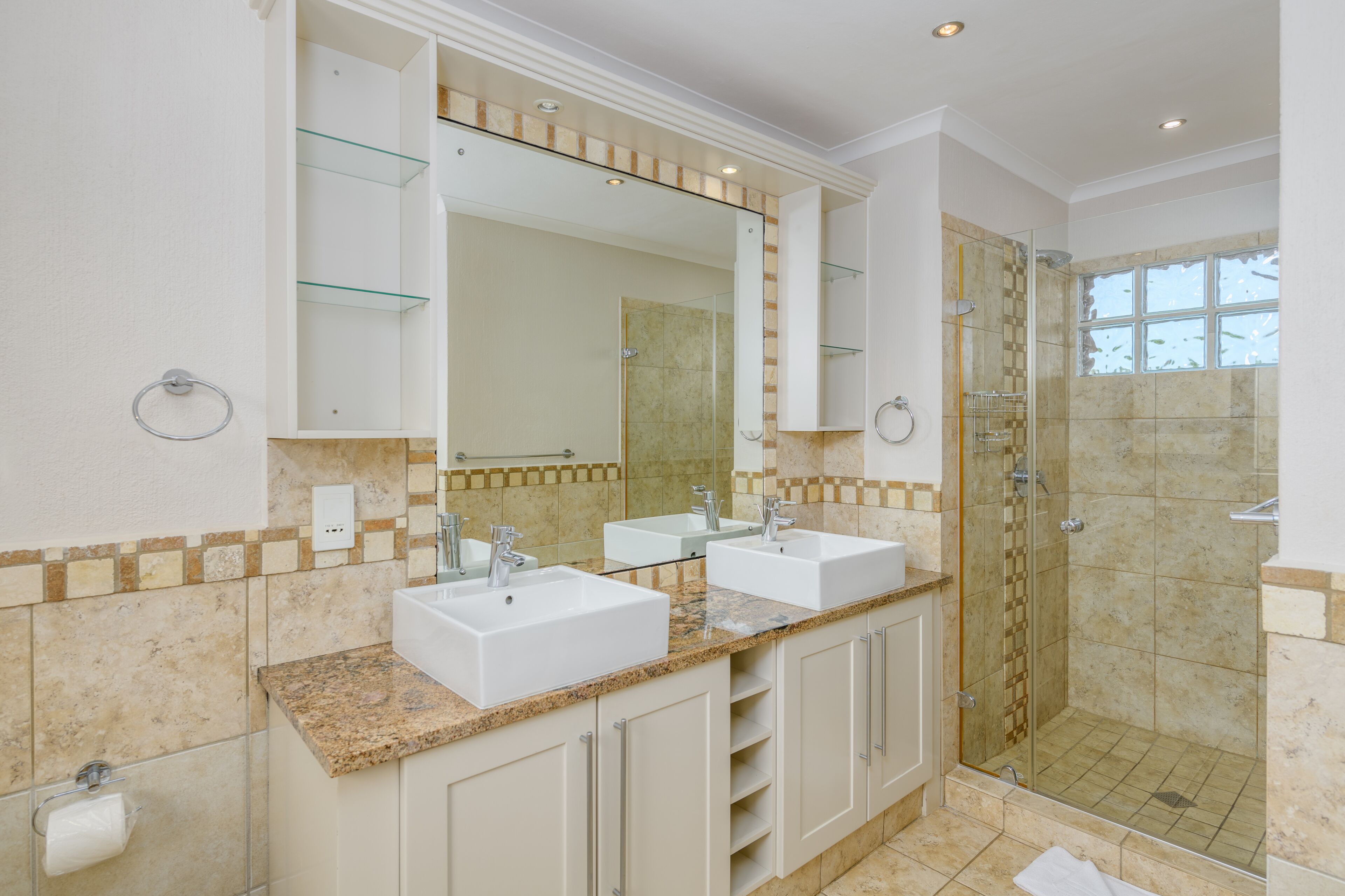 A modern bathroom with two sinks, a large mirror, and a glass-enclosed shower.
