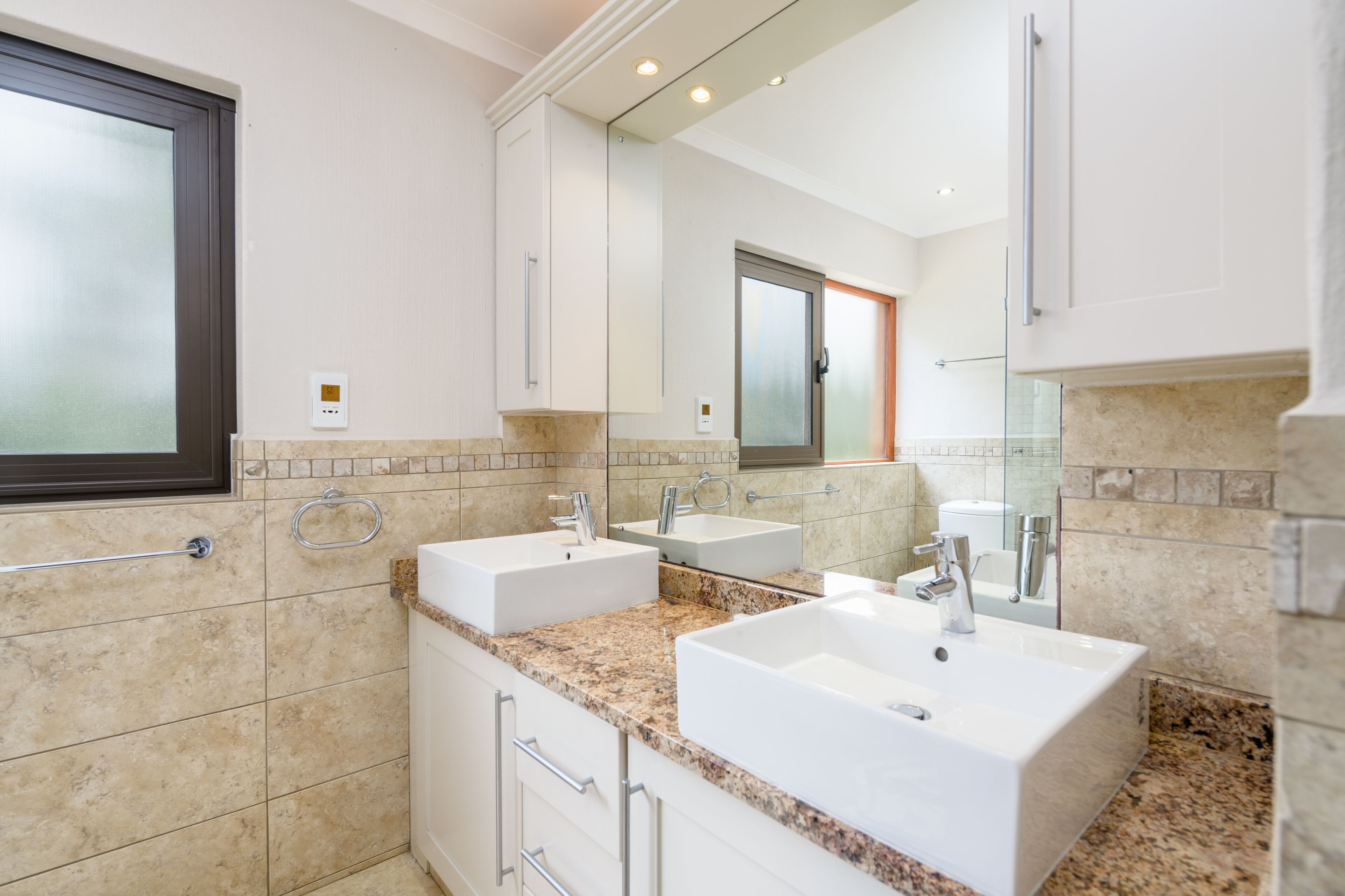 Un baño moderno con dos lavamanos, un espejo grande y una ventana.