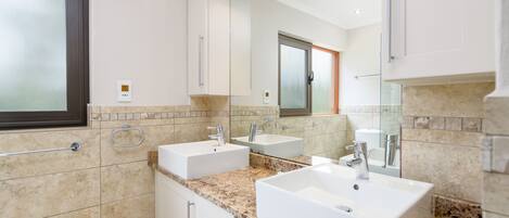 Un baño moderno con dos lavamanos, un espejo grande y una ventana.