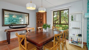 A dining area with a wooden table, four chairs, a potted plant, and a white bookshelf. - San Lameer Villa Rentals 1924 (Southbroom)