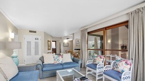 Una sala de estar con un sofá azul, sillones blancos, una mesa de centro y un ventanal con cortinas.