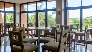 A spacious indoor area with large windows, multiple tables and chairs, and a view of palm trees and buildings outside. - San Lameer Villa Rentals 14105 (Southbroom)