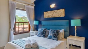 A bedroom with a bed, two bedside tables, a window with curtains, and a wall-mounted light fixture. - San Lameer Villa Rentals 1929 (Southbroom)