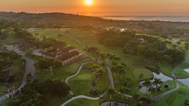 An aerial view of a golf course with a clubhouse, water hazards, and a sunset in the background. - San Lameer Villa Rentals 1929 (Southbroom)
