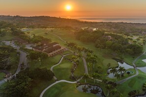 An aerial view of a golf course with a clubhouse, water hazards, and a sunset in the background. - San Lameer Villa Rentals 1929 (Southbroom)