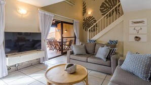 A living room with a sofa, a coffee table, a TV, and a staircase leading to a balcony. - San Lameer Villa Rentals 1929 (Southbroom)