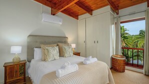 A bedroom with a bed, two nightstands, an air conditioner, a window with a view, and a balcony with a wicker stool. - San Lameer Villa Rentals 3506 (Southbroom)