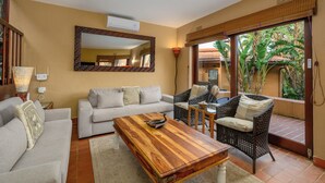 A living room with a sofa, a wooden coffee table, wicker chairs, a large mirror, and a view of greenery through a glass door. - San Lameer Villa Rentals 3506 (Southbroom)