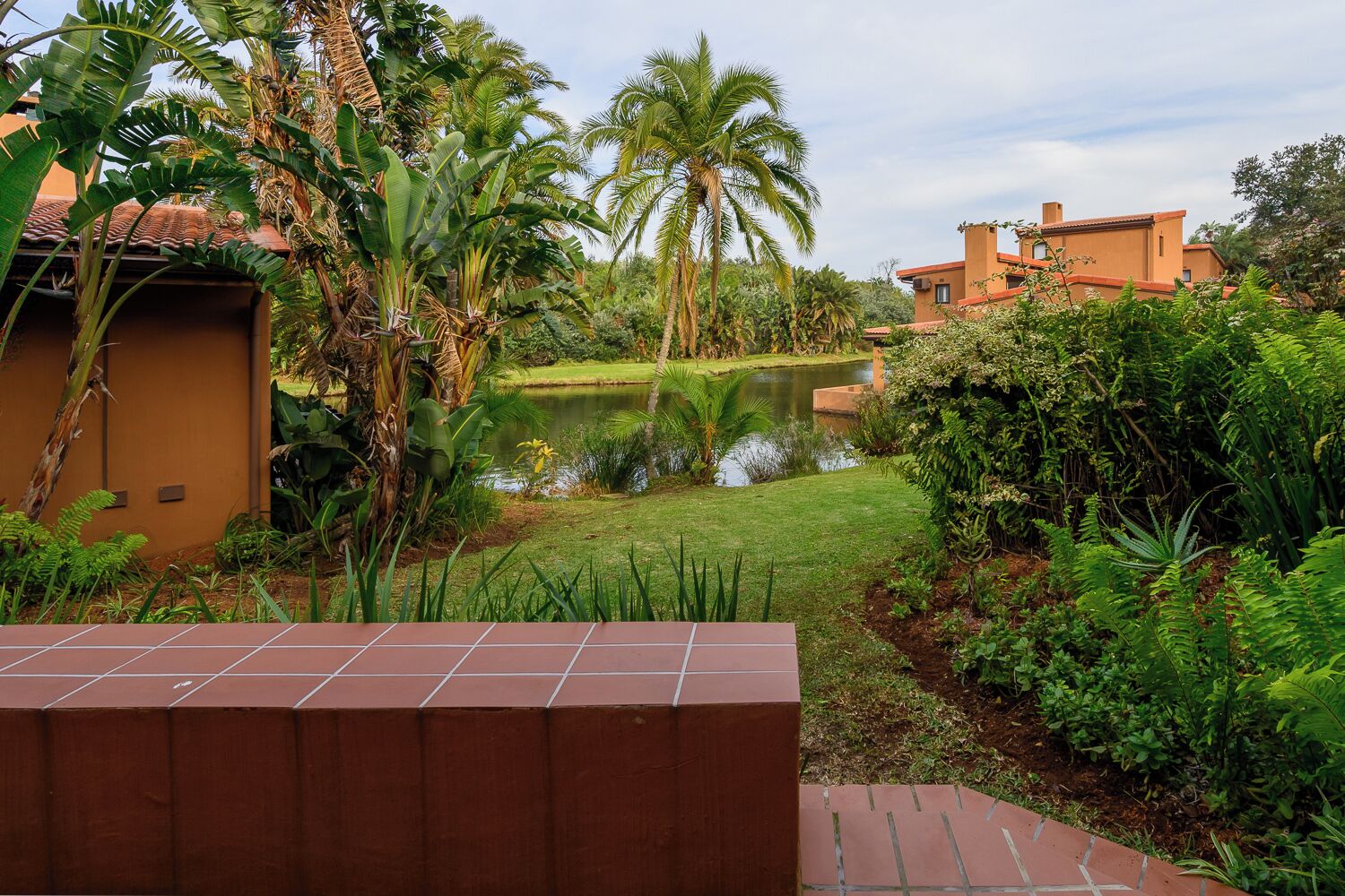 A courtyard with a pond, lush greenery, and a building with a tiled roof.