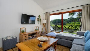A living room with a TV, wooden entertainment unit, and a large window with a view of a golf course. - San Lameer Villa Rentals 10432 (Southbroom)