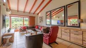 Un vaste espace de vie comprenant un grand canapé, un fauteuil rouge et un meuble en bois. Une grande fenêtre offre une vue sur la verdure environnante.