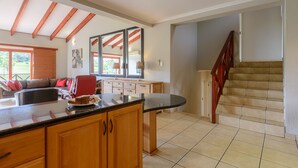Une cuisine spacieuse, dotée de meubles en bois, d’un grand îlot central et offrant une vue sur un espace de vie comprenant un canapé et un fauteuil rouge.