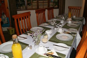 Uma mesa de jantar posta para refeição, com pratos, talheres e uma garrafa de suco de laranja.