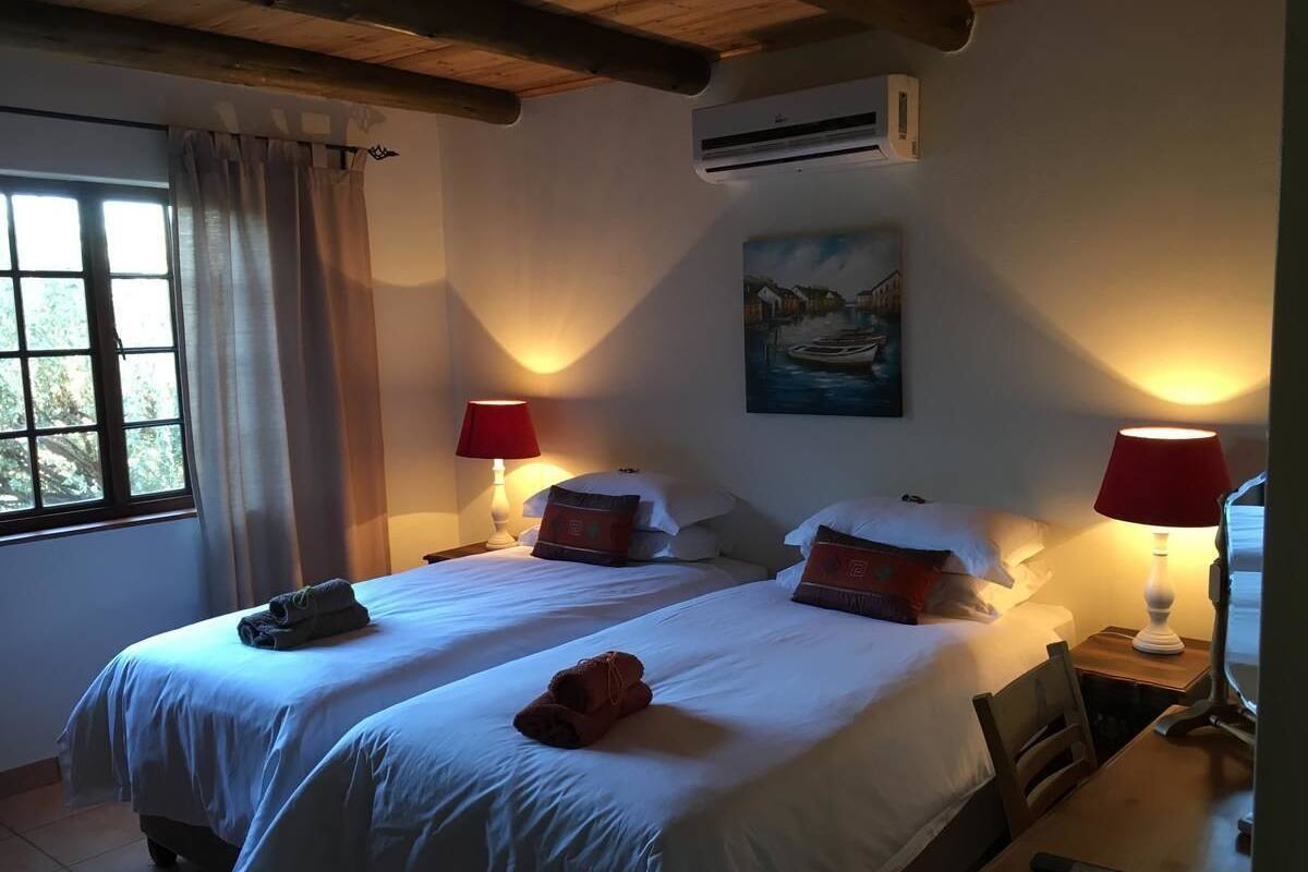 A double bed with white linens, two bedside lamps, a painting on the wall, and a window with curtains.