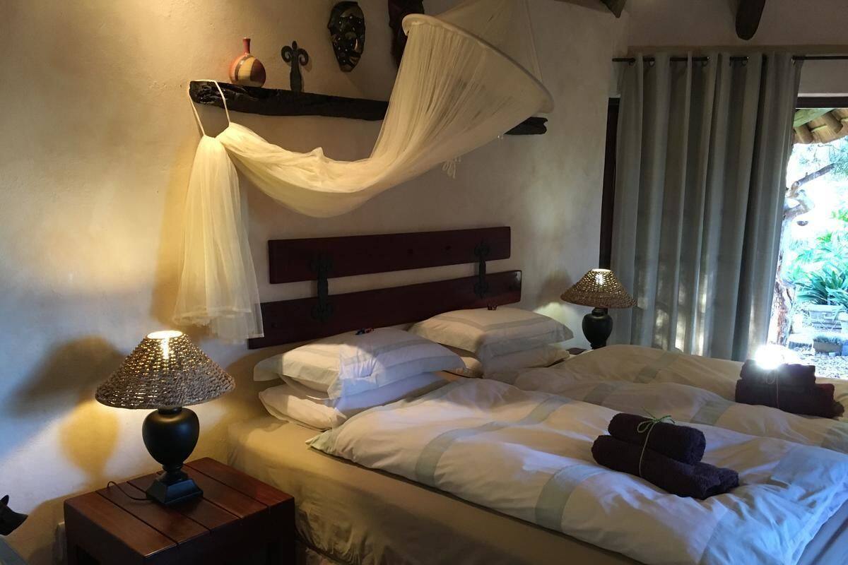 A bedroom with a bed, two bedside tables with lamps, a canopy, and a view of greenery outside.