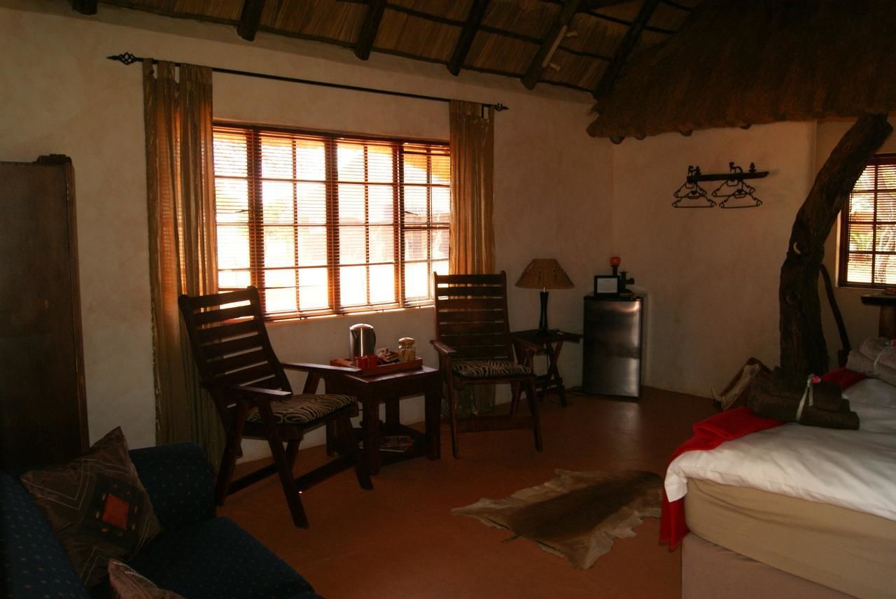 Um quarto aconchegante com uma cama, duas cadeiras de madeira, uma mesa pequena, um abajur e uma janela com cortinas.