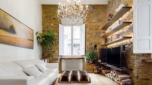 A modern living room with a stone wall, a white sofa, a fur throw, a chandelier, and a TV. - Luxury 2 Bedroom Apartment with Hot Tub - Florence City Center (Florence)