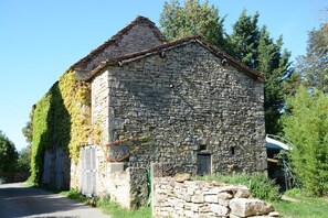 Un edificio de piedra con techo inclinado, una puerta pequeña y contraventanas.