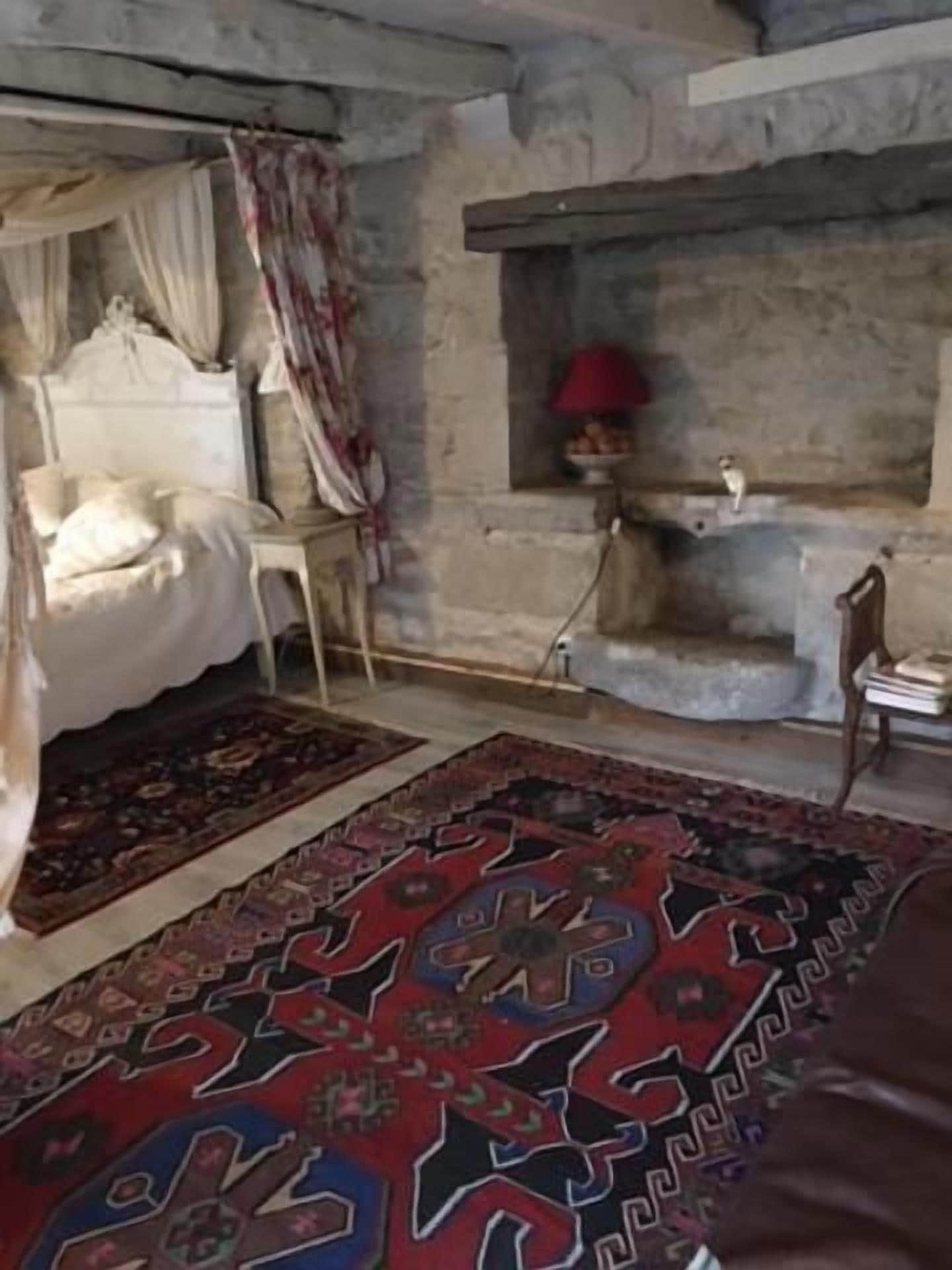 Une chambre à coucher avec un lit, une table de chevet, une lampe rouge et un mur en pierre.