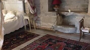 Une chambre à coucher avec un lit, une table de chevet, une lampe rouge et un mur en pierre.