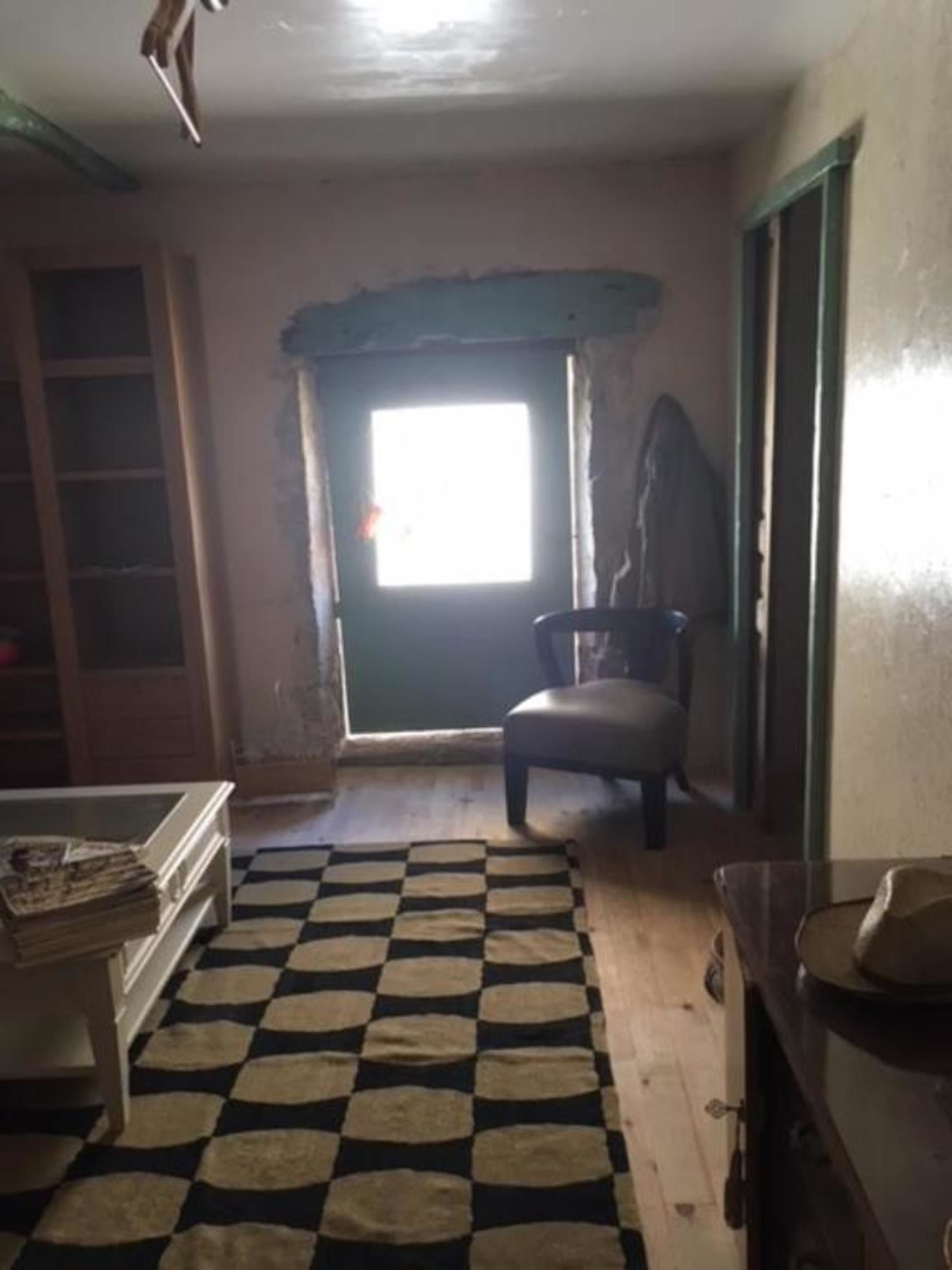 A room with a checkered rug, a chair, a table with a hat, and a window with a view.