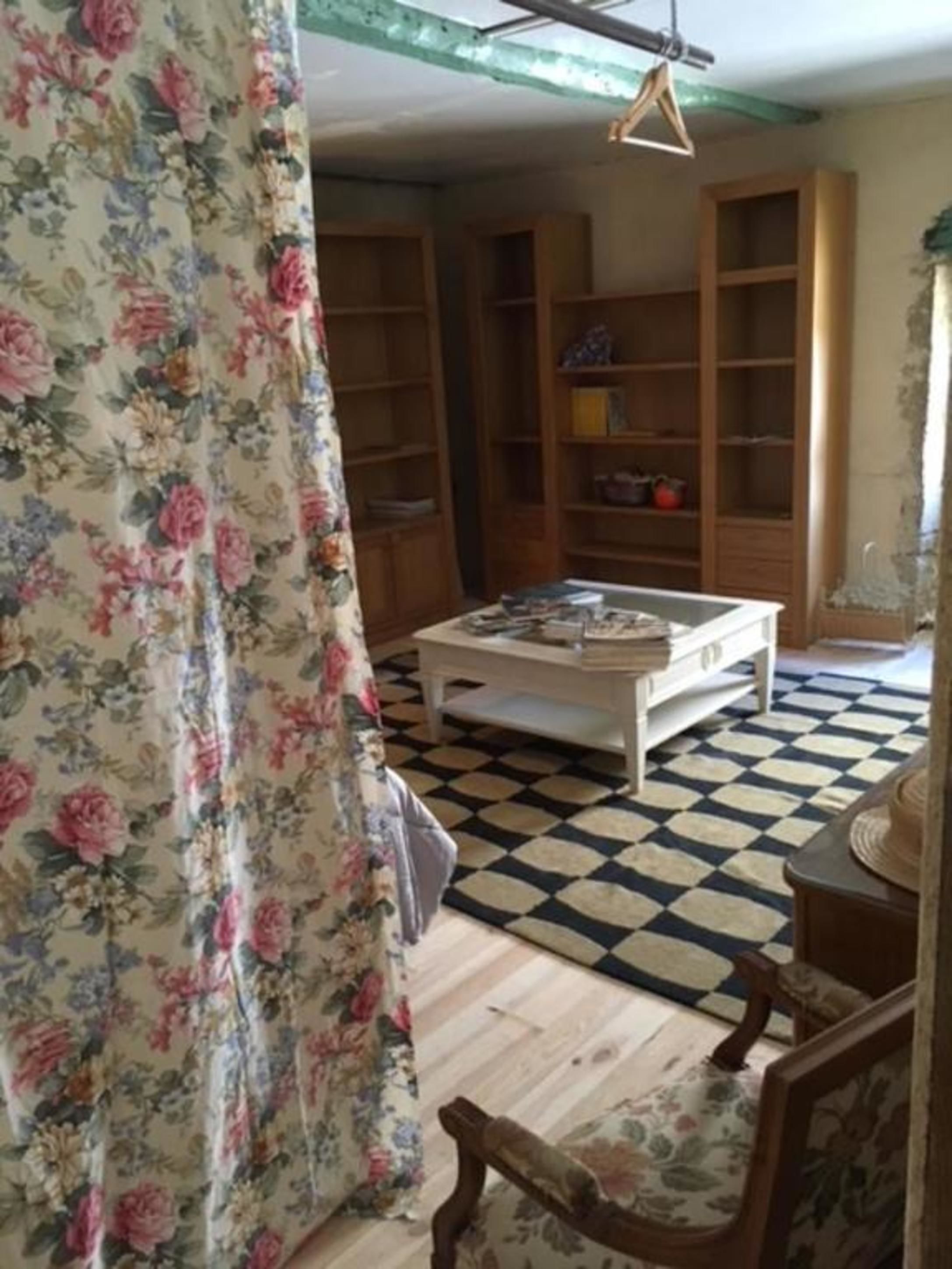 Een woonkamer met een zwart-wit geruite vloer, bloemen gordijnen, houten boekenkasten en een witte salontafel.