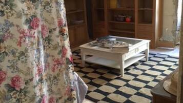 Een woonkamer met een zwart-wit geruite vloer, bloemen gordijnen, houten boekenkasten en een witte salontafel.