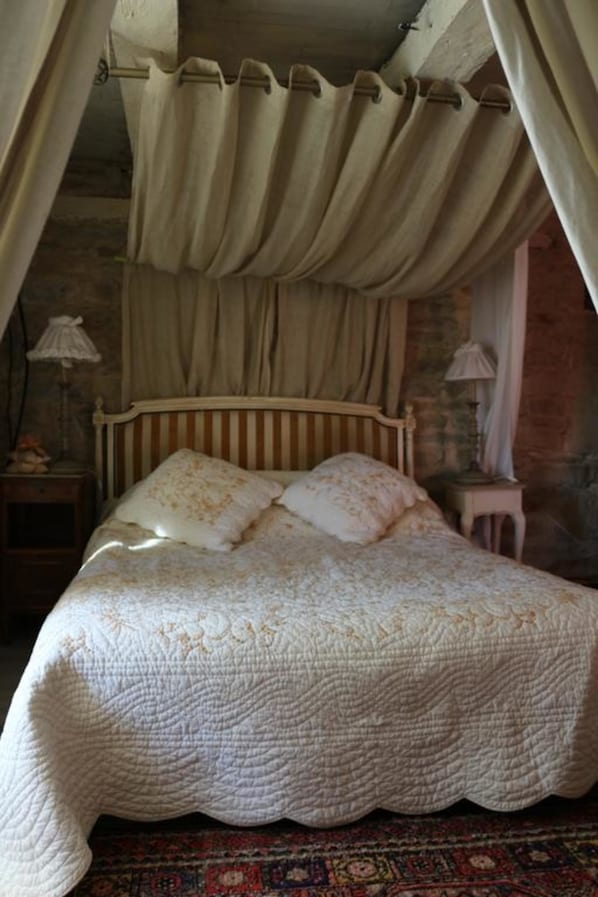 A bed with a canopy, a nightstand, a lamp, and a patterned rug.