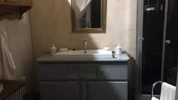 A bathroom with a dark tiled floor, a white sink with a mirror above it, and a shower area with a glass door.