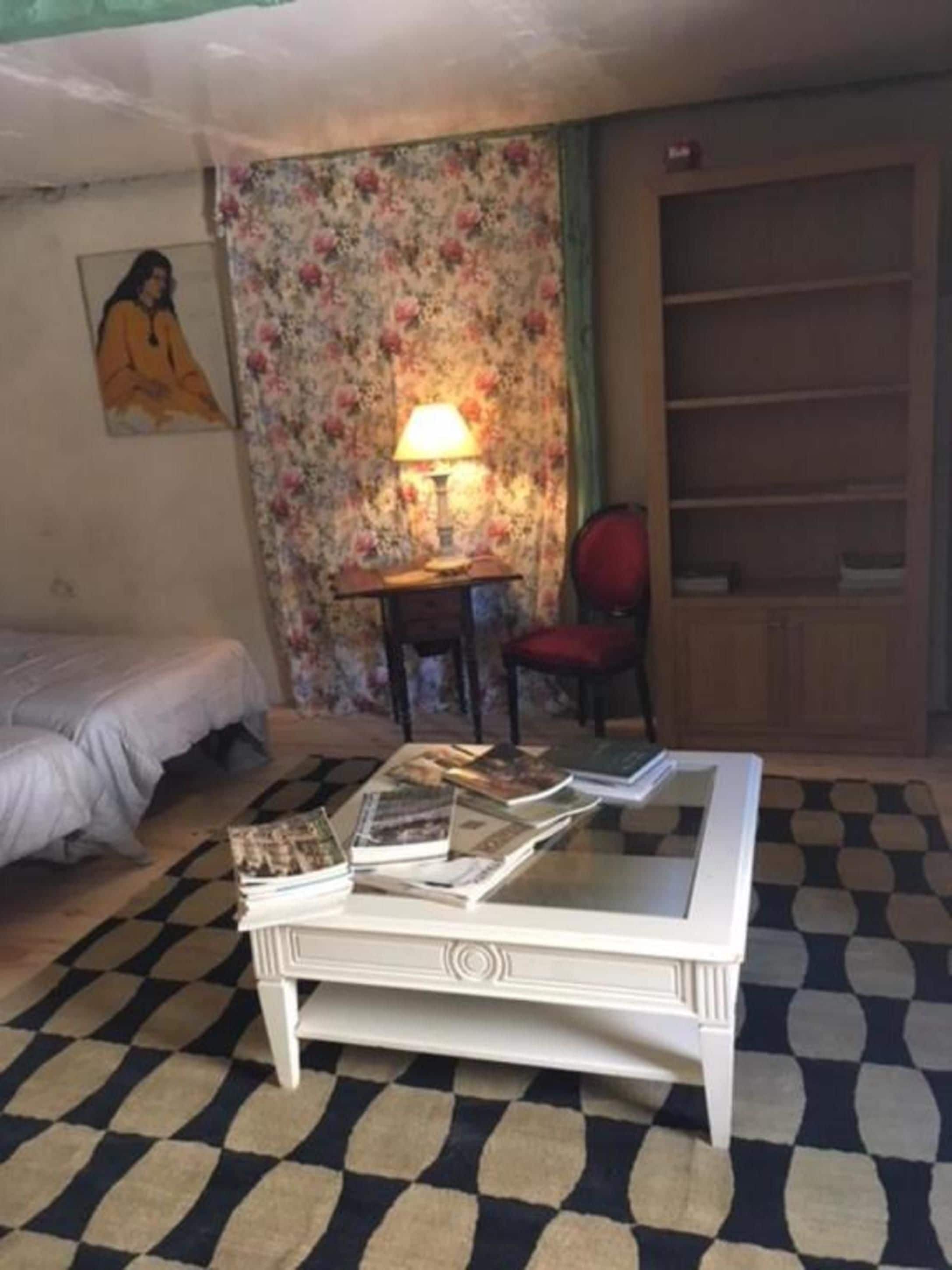 Et værelse med en seng, et lille bord med bøger, en stol, en lampe og en bogreol.