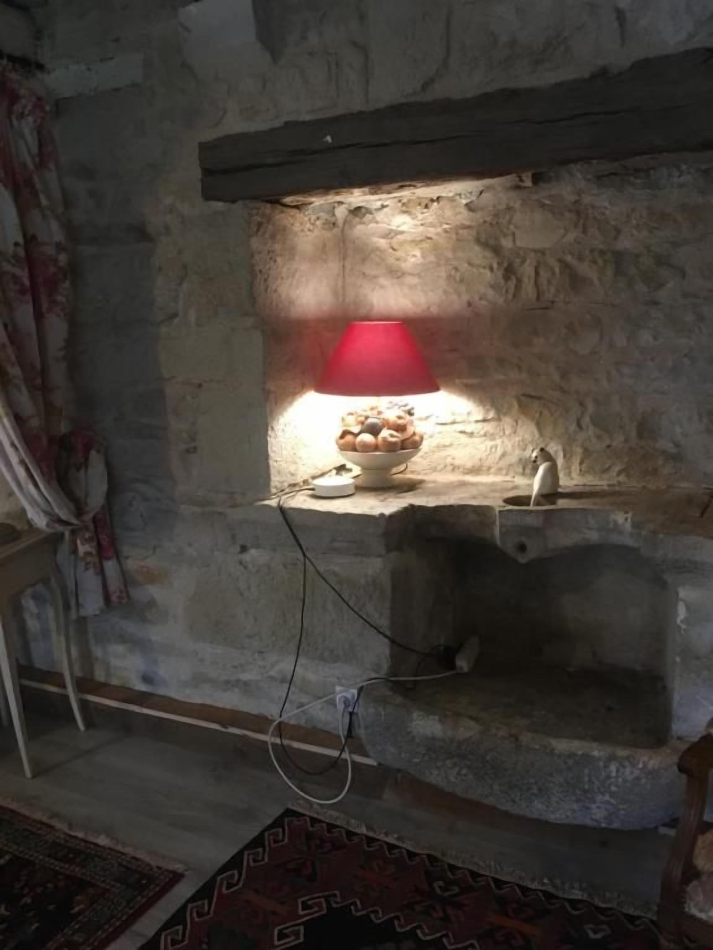 A stone wall with a shelf holding a bowl of snacks and a red lamp.
