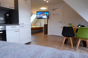 Una cocina moderna con horno integrado, un comedor con mesa y sillas de madera y un televisor montado en la pared.