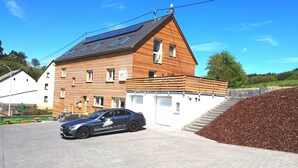 A two-story building with a sloped roof, solar panels, and a car parked in front. - Speedys Gästehaus am Brünnchen (Herresbach)