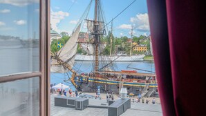 A view from a window overlooking a dock with a large sailing ship, a small boat, and a building with a flag. - Hotel Gamla Stan, BW Signature Collection (Stockholm)