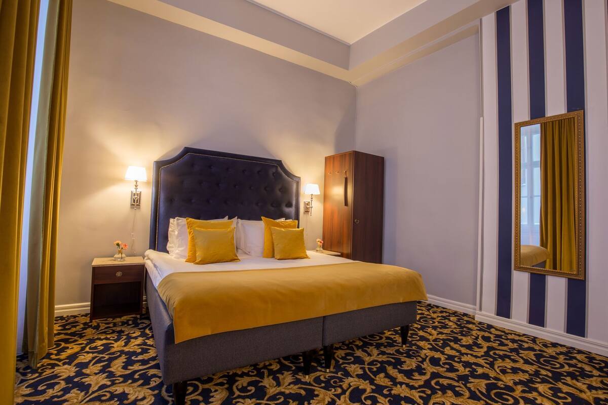 A hotel room with a large bed, a wardrobe, a nightstand, and a mirror.