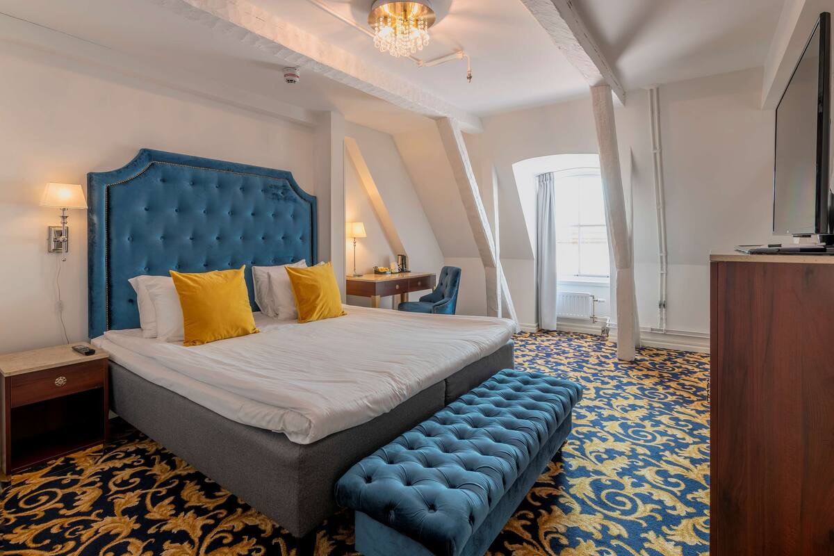 A bedroom with a large bed, a bench, a desk, and a television.