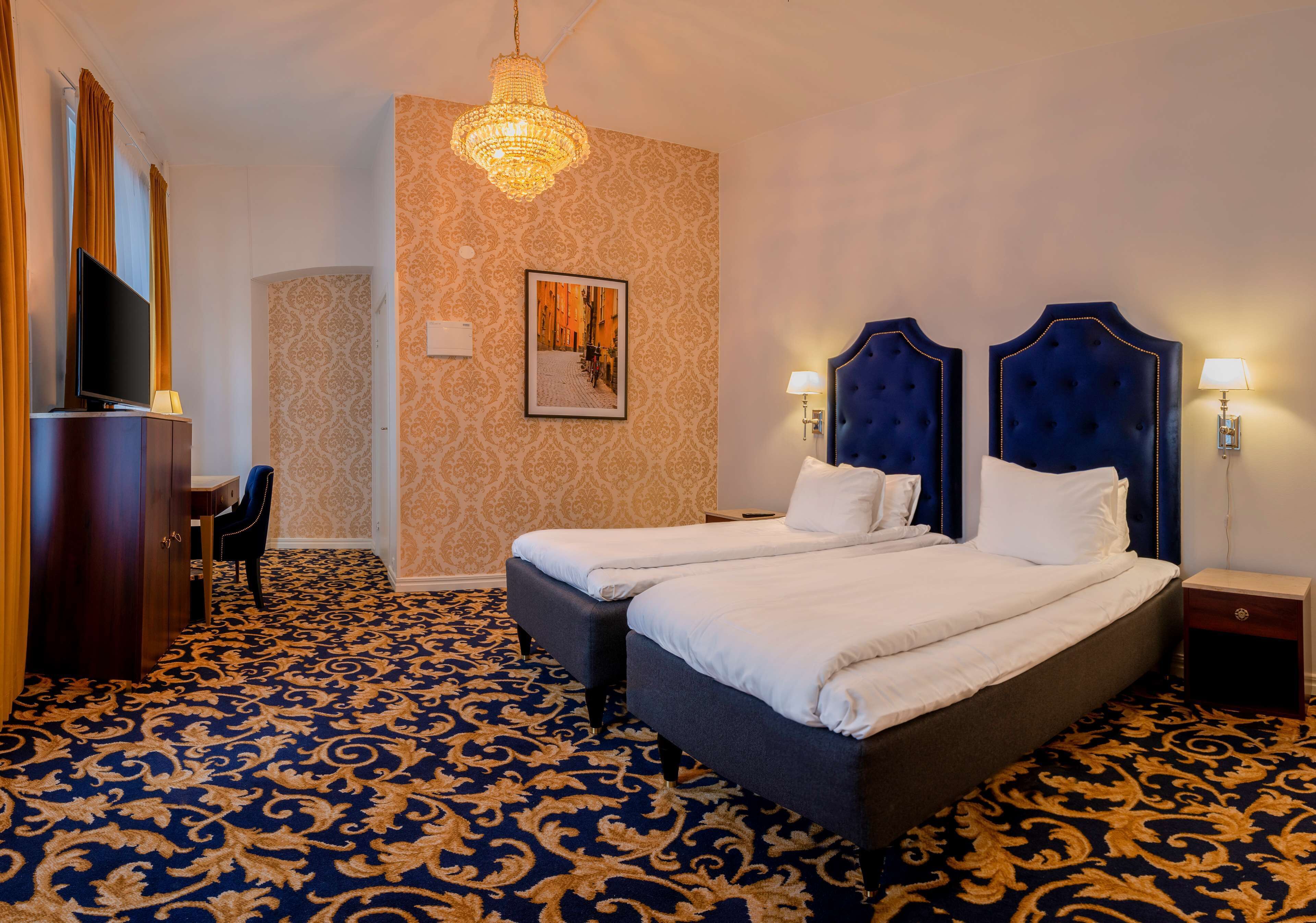 Ett hotellrum med en stor säng, två sängbord, en tv och en kristallkrona.