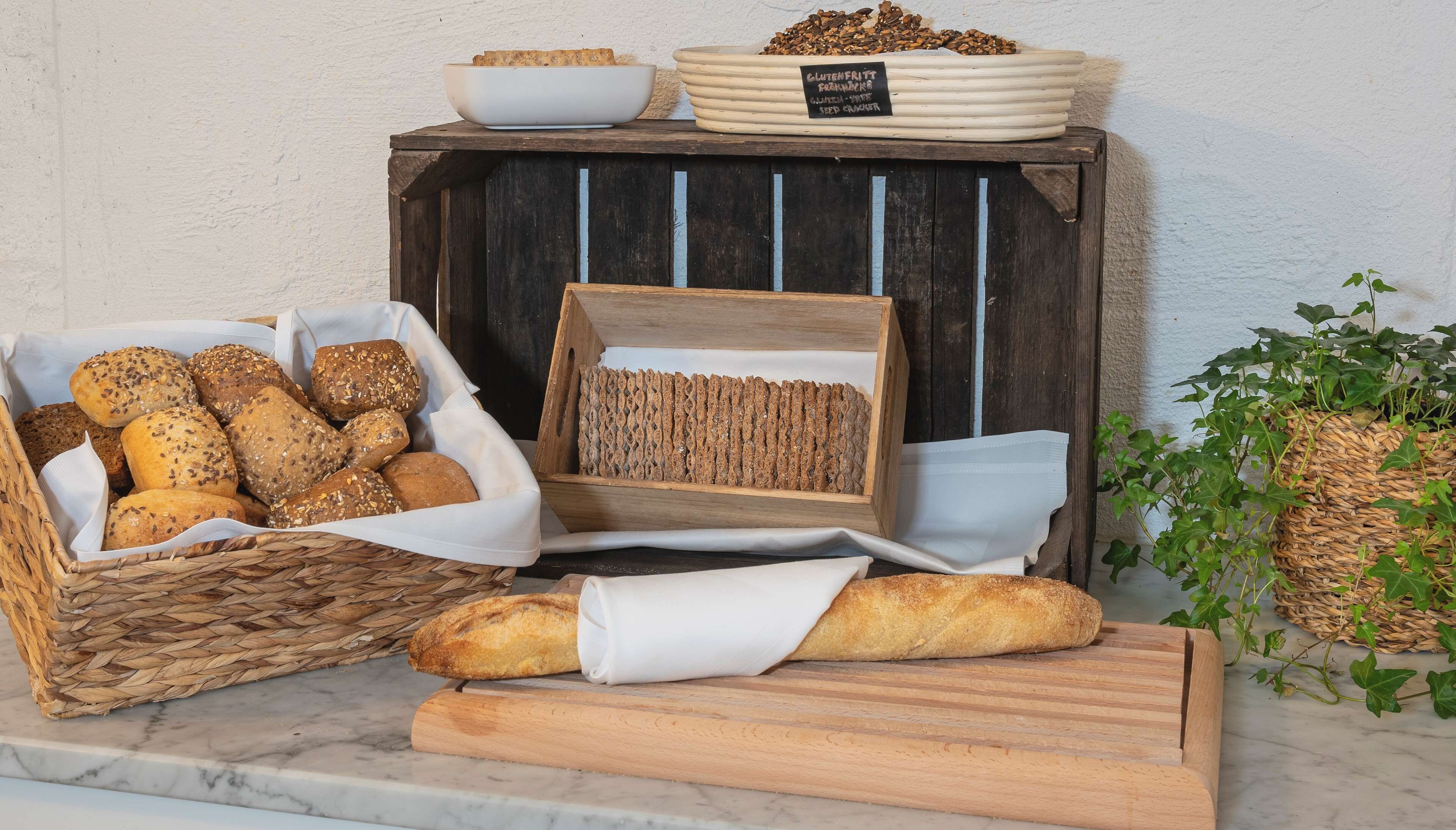 A display of various breads and seeds on a wooden table against a white wall.