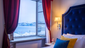 A hotel room with a bed, a window with curtains, a nightstand with a lamp, and a view of a snowy landscape. - Hotel Gamla Stan, BW Signature Collection (Stockholm)