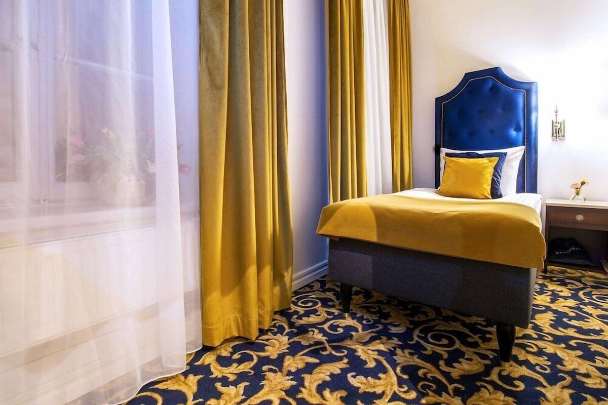 A hotel room with a bed, curtains, and a patterned carpet.