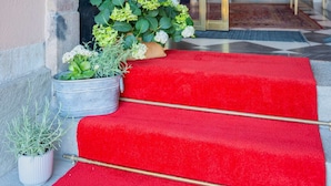 A hotel entrance with a red carpet, potted plants, and a staircase leading inside. - Hotel Gamla Stan, BW Signature Collection (Stockholm)