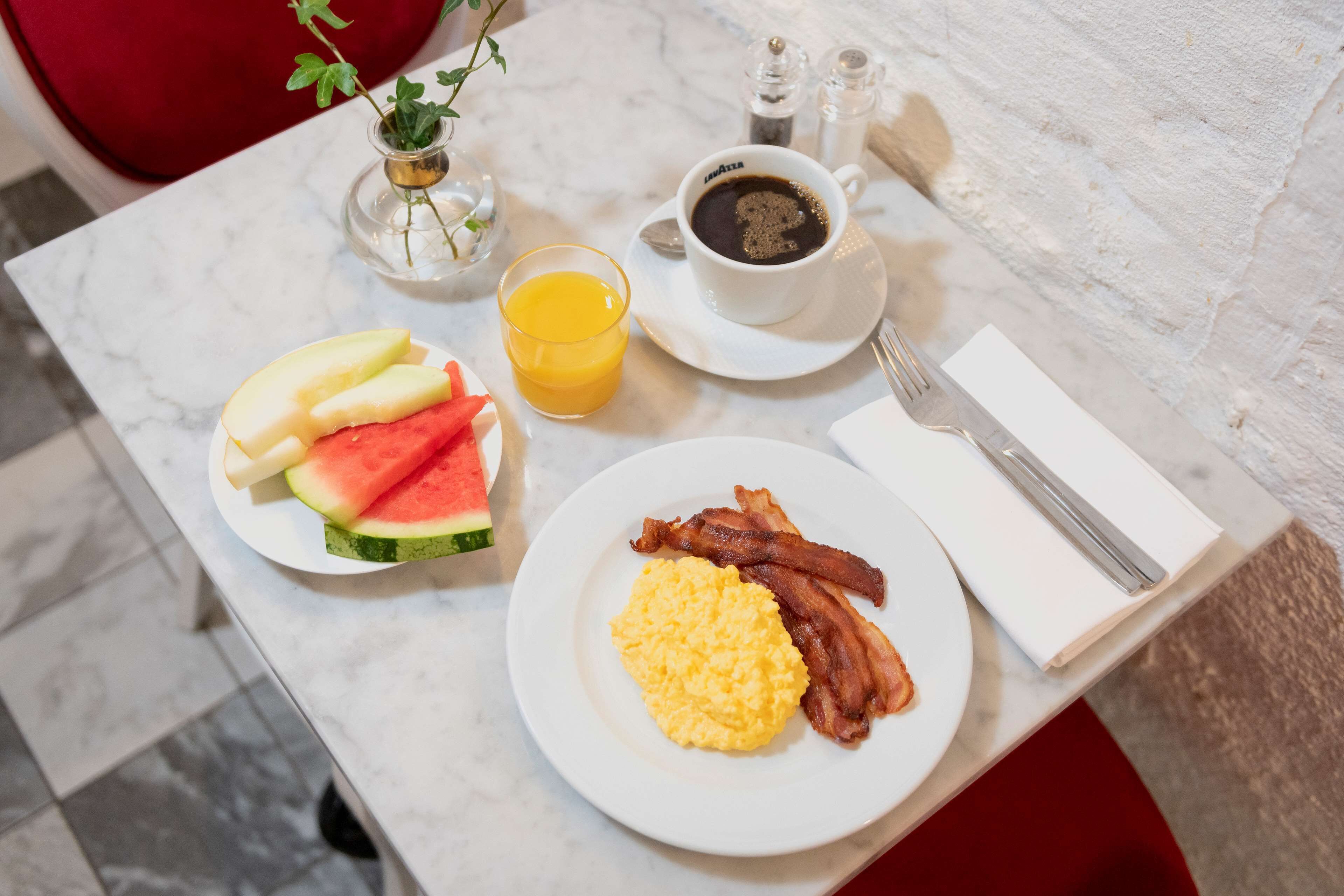 A breakfast table with a plate of eggs, bacon, and watermelon, a cup of coffee, and a glass of orange juice.